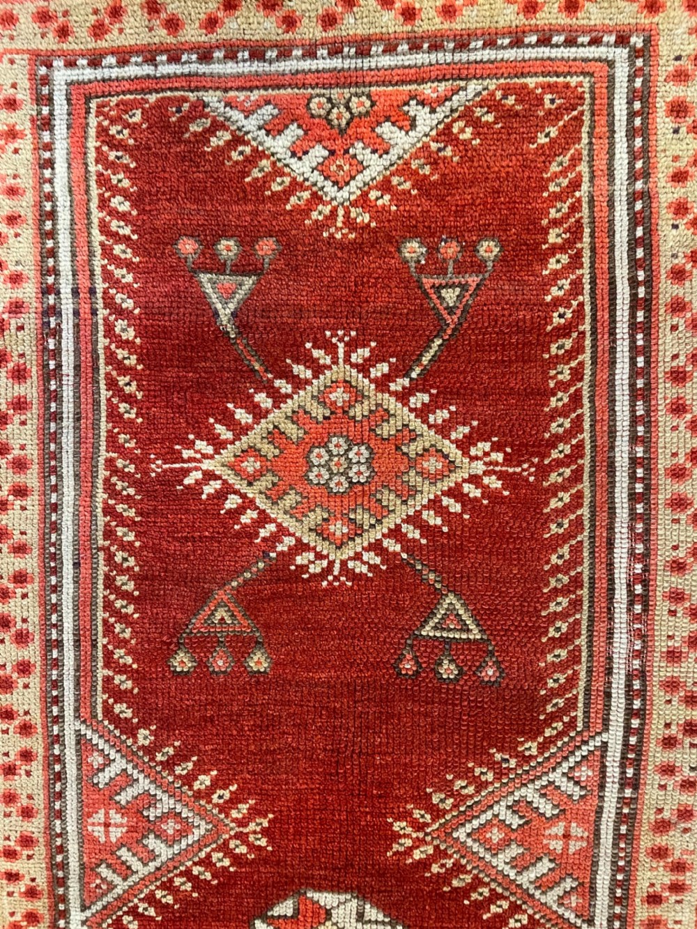 A rectangular hand-knotted Anatolian Melas wool rug featuring a red central pointed mihrab field framed by broad geometric patterned borders in cream, ochre, and dark brown. View II