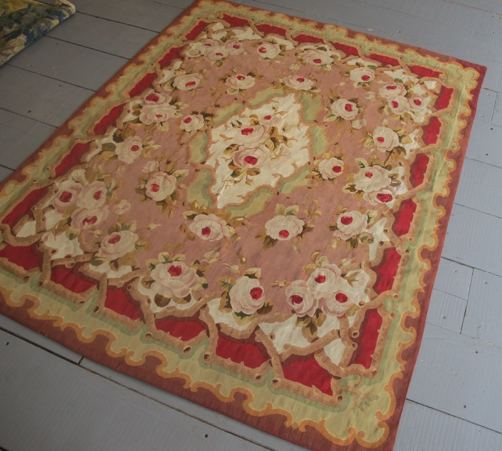 A rectangular antique French Aubusson flatweave wool rug featuring a central floral medallion surrounded by rose motifs, scrollwork borders, and shades of pink, red, green, and cream. View III