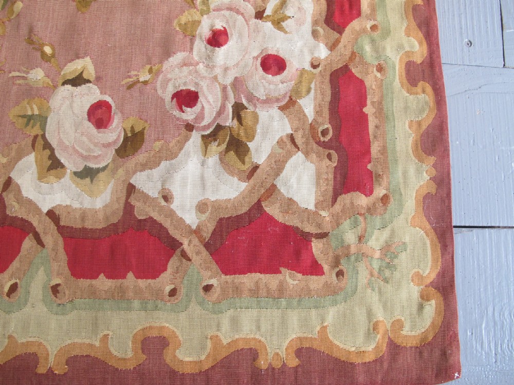 A rectangular antique French Aubusson flatweave wool rug featuring a central floral medallion surrounded by rose motifs, scrollwork borders, and shades of pink, red, green, and cream. View IV