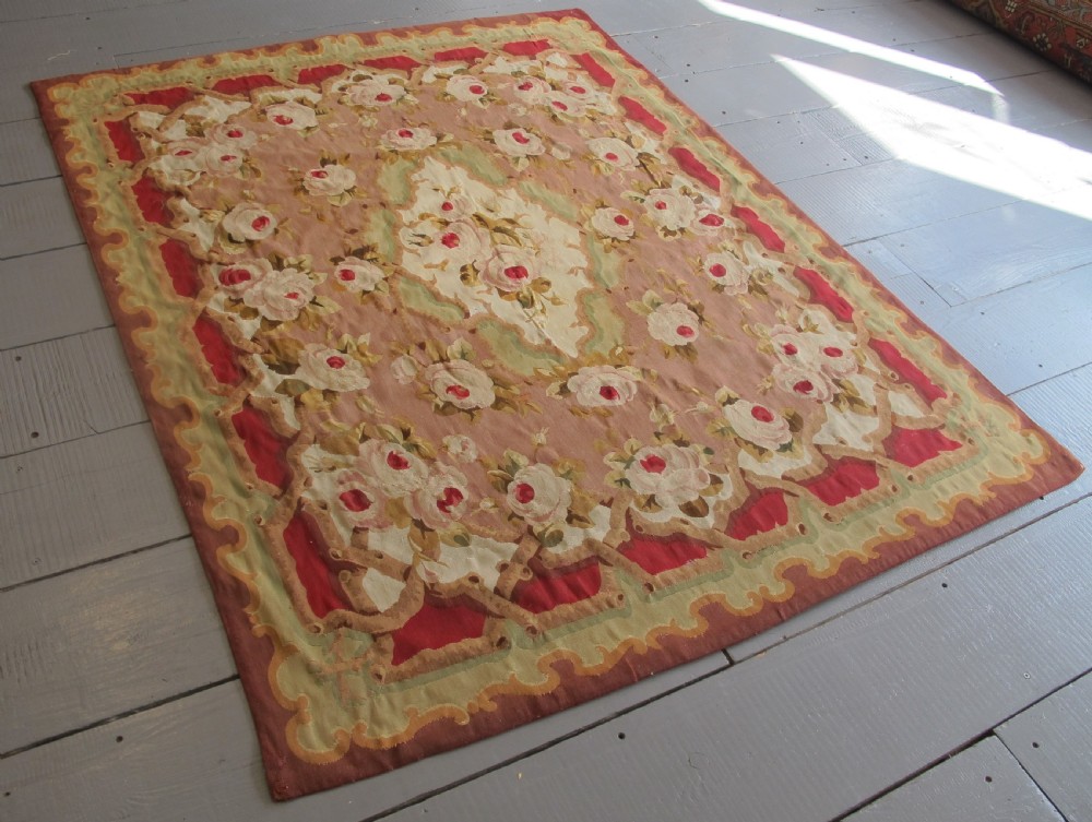 A rectangular antique French Aubusson flatweave wool rug featuring a central floral medallion surrounded by rose motifs, scrollwork borders, and shades of pink, red, green, and cream. View IX