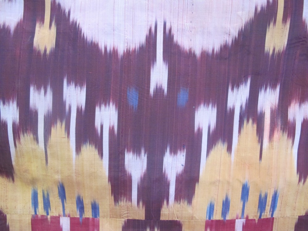 A rectangular handwoven silk ikat textile panel displaying repeating floral and botanical motifs in shades of burgundy, magenta, pink, and ochre yellow. View IV