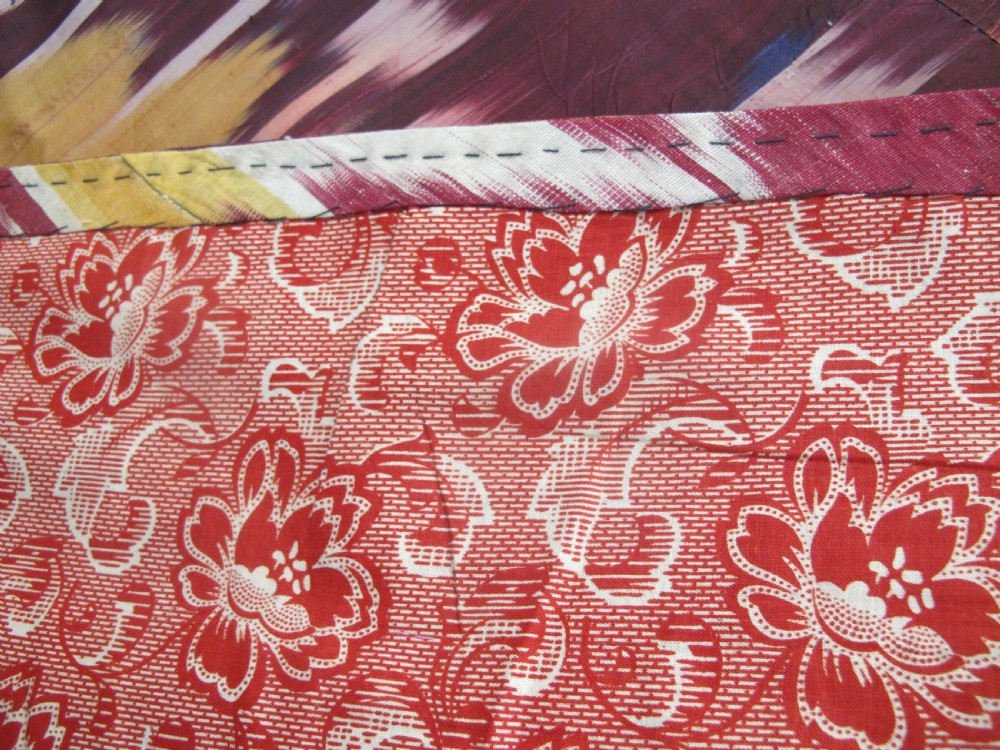A rectangular handwoven silk ikat textile panel displaying repeating floral and botanical motifs in shades of burgundy, magenta, pink, and ochre yellow. View VII