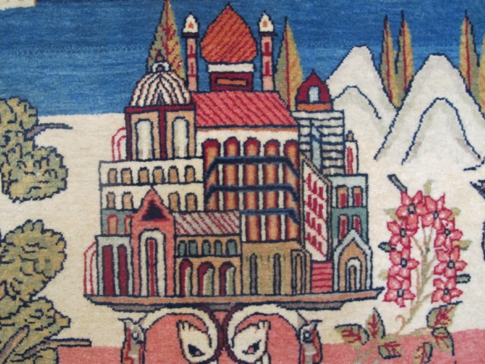 A pair of small Persian Kashan pictorial wool rugs featuring woven architectural scenes, trees, and animals set against terracotta red, cream, and navy blue backgrounds. View IV