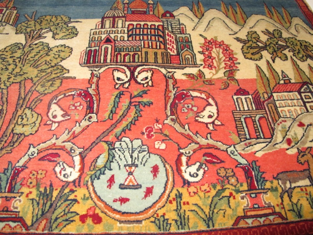 A pair of small Persian Kashan pictorial wool rugs featuring woven architectural scenes, trees, and animals set against terracotta red, cream, and navy blue backgrounds. View VI
