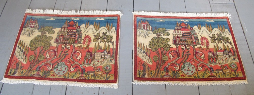 A pair of small Persian Kashan pictorial wool rugs featuring woven architectural scenes, trees, and animals set against terracotta red, cream, and navy blue backgrounds. View VII