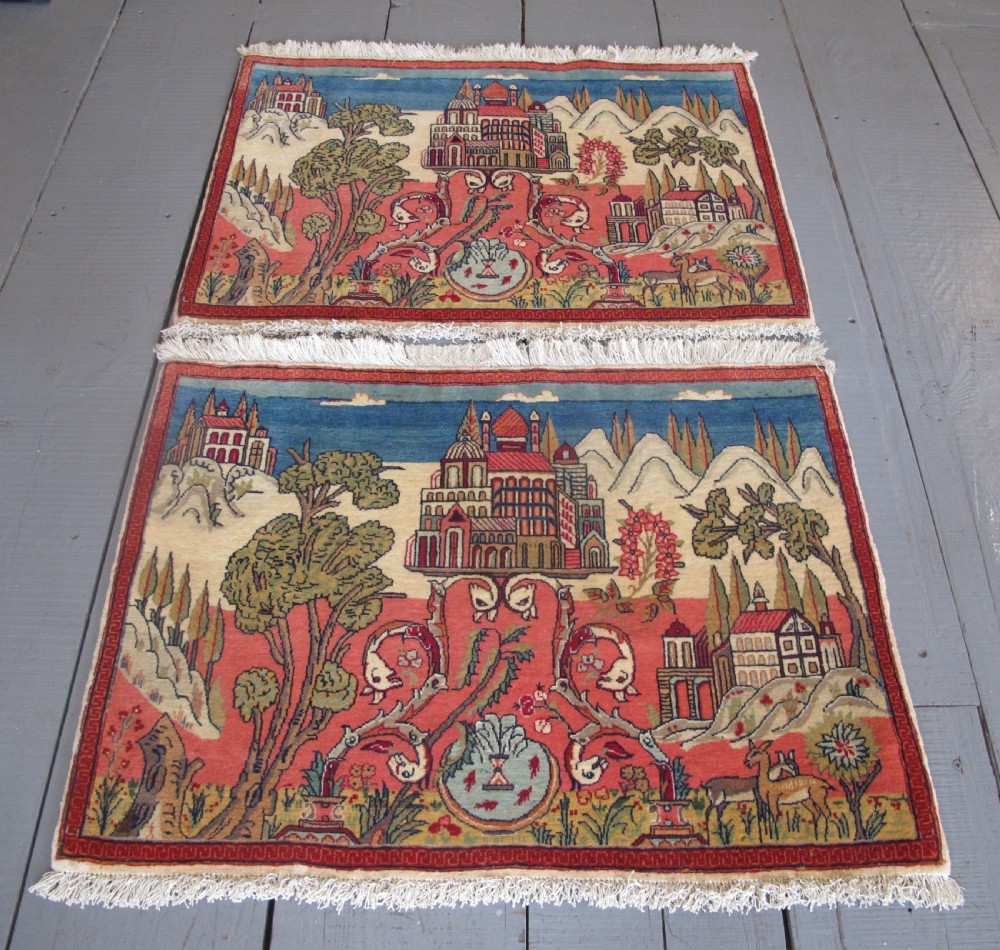 A pair of small Persian Kashan pictorial wool rugs featuring woven architectural scenes, trees, and animals set against terracotta red, cream, and navy blue backgrounds. View XI