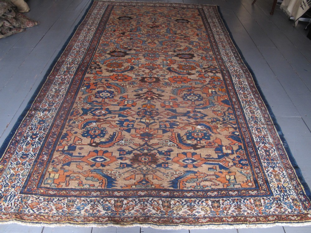 An antique hand-knotted Hamadan carpet featuring intricate geometric and floral patterns in terracotta, indigo blue, and tan hues.