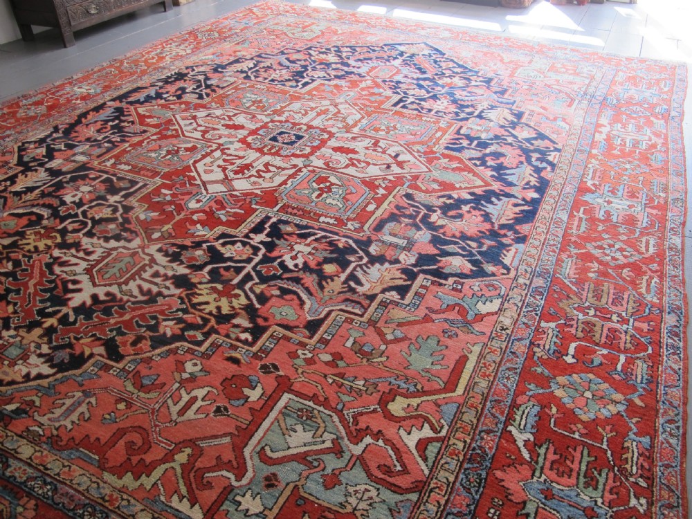 A large antique Persian Heriz carpet featuring a central geometric medallion surrounded by stylized floral motifs in terracotta, navy blue, and cream tones. View III