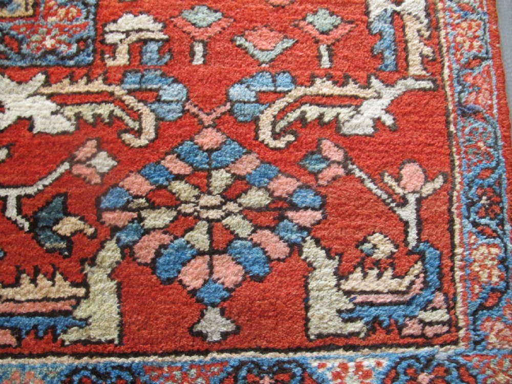 A large antique Persian Heriz carpet featuring a central geometric medallion surrounded by stylized floral motifs in terracotta, navy blue, and cream tones. View IV