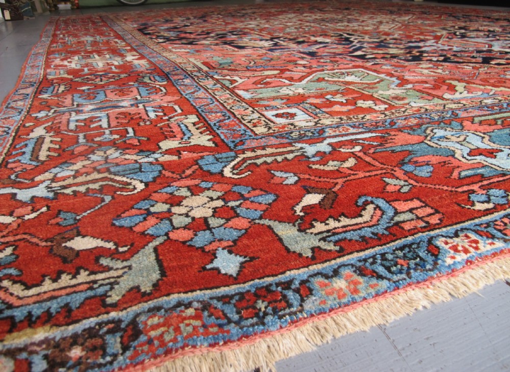 A large antique Persian Heriz carpet featuring a central geometric medallion surrounded by stylized floral motifs in terracotta, navy blue, and cream tones. View VIII