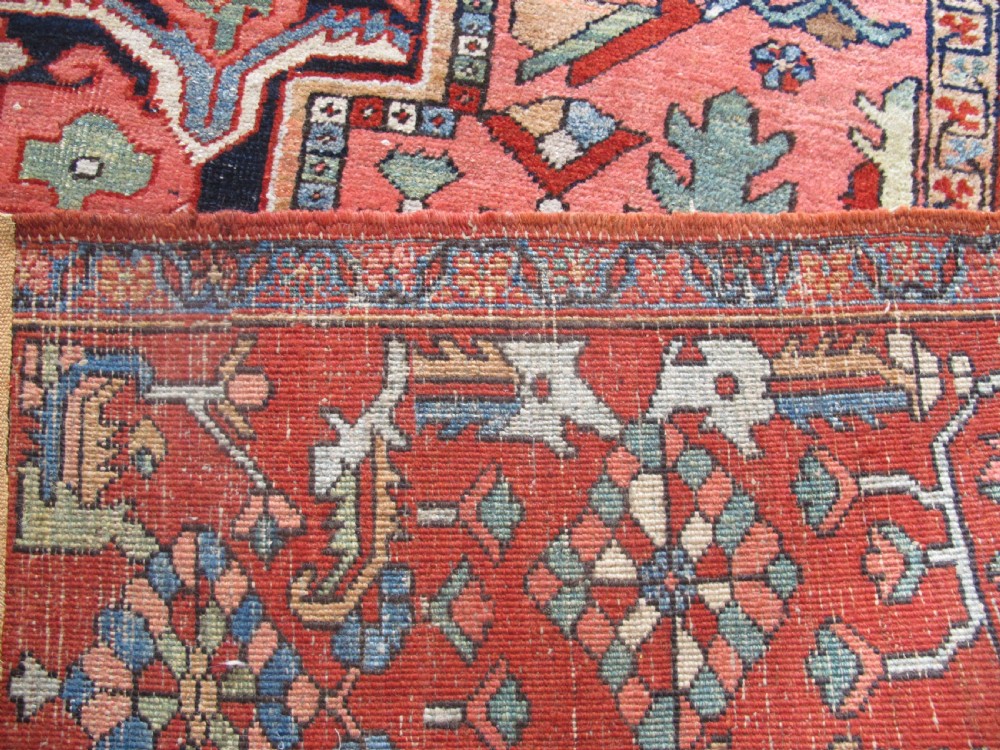 A large antique Persian Heriz carpet featuring a central geometric medallion surrounded by stylized floral motifs in terracotta, navy blue, and cream tones. View IX