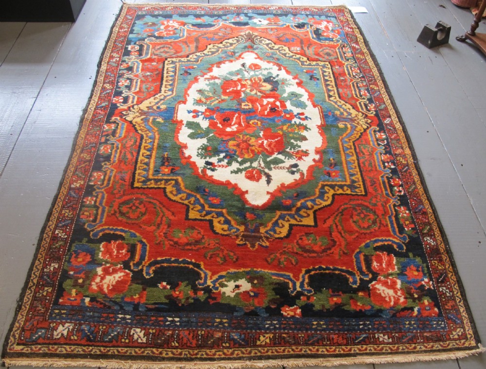 An antique hand-knotted Persian Bakhtiari wool rug featuring a central white floral medallion surrounded by terracotta red, blue, green, and dark navy borders.