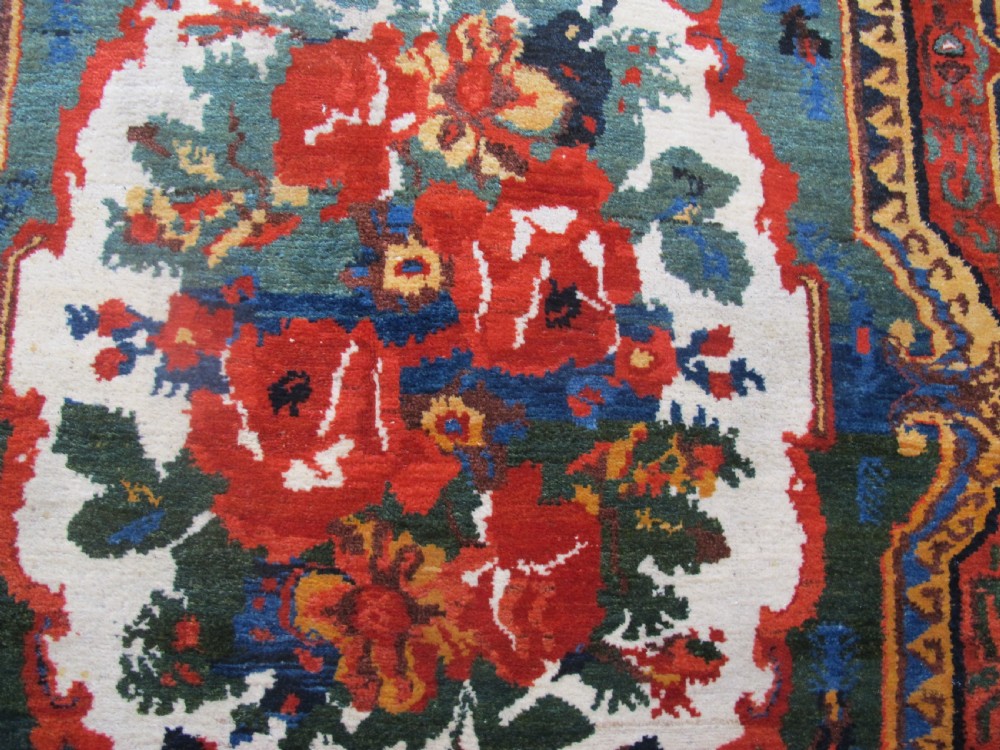 An antique hand-knotted Persian Bakhtiari wool rug featuring a central white floral medallion surrounded by terracotta red, blue, green, and dark navy borders. View III