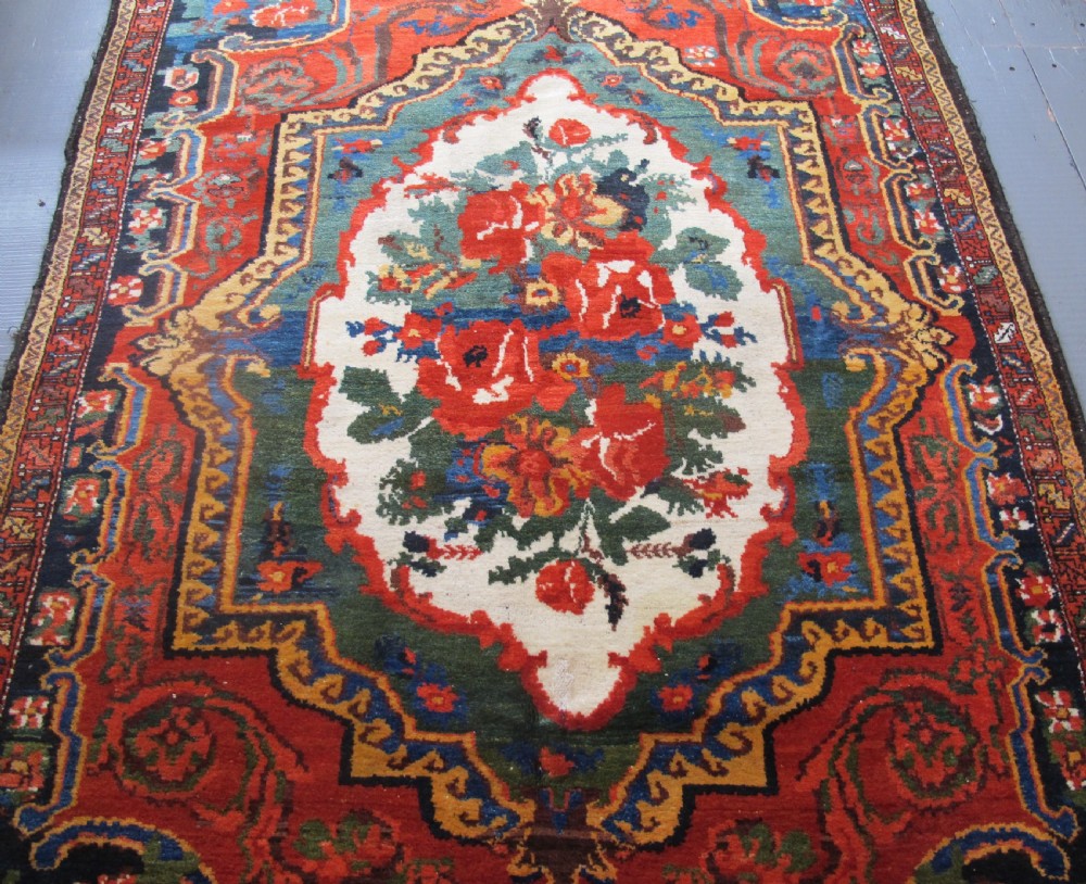An antique hand-knotted Persian Bakhtiari wool rug featuring a central white floral medallion surrounded by terracotta red, blue, green, and dark navy borders. View IV