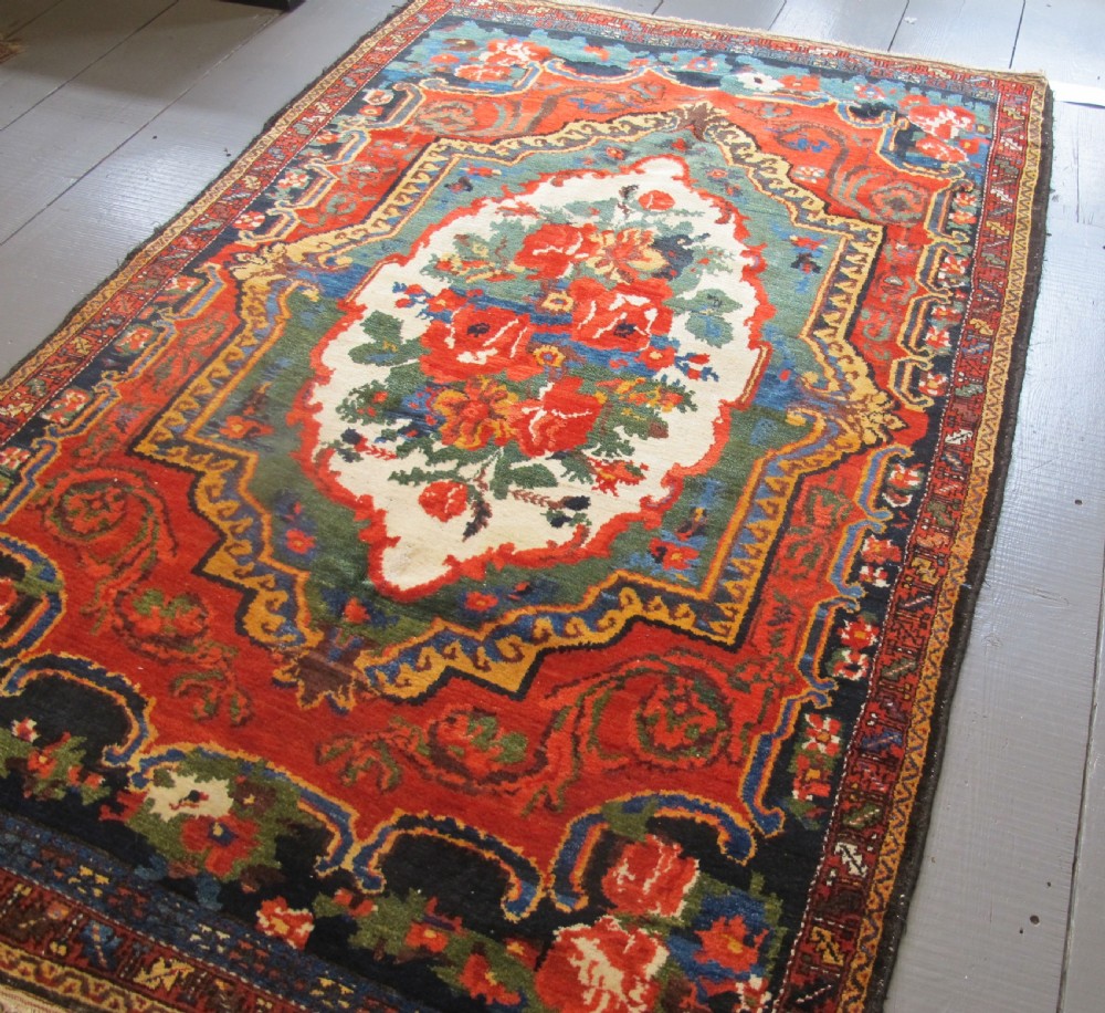 An antique hand-knotted Persian Bakhtiari wool rug featuring a central white floral medallion surrounded by terracotta red, blue, green, and dark navy borders. View V