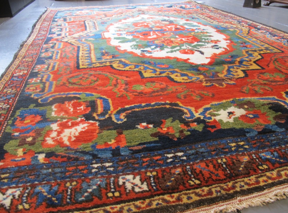 An antique hand-knotted Persian Bakhtiari wool rug featuring a central white floral medallion surrounded by terracotta red, blue, green, and dark navy borders. View VI