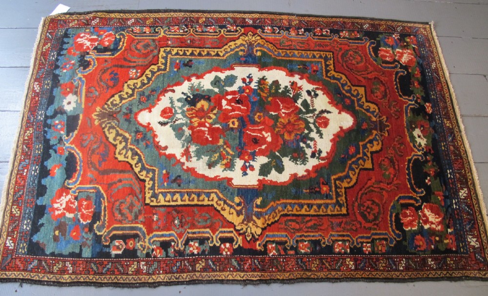 An antique hand-knotted Persian Bakhtiari wool rug featuring a central white floral medallion surrounded by terracotta red, blue, green, and dark navy borders. View VII