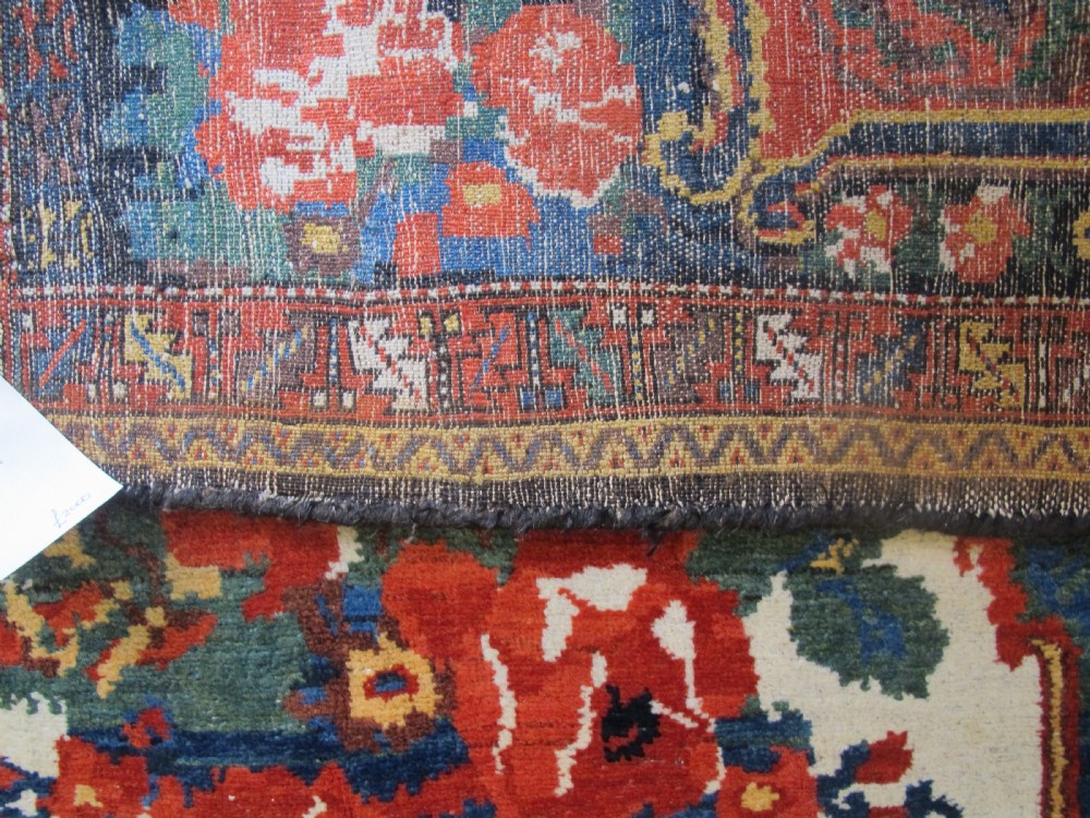 An antique hand-knotted Persian Bakhtiari wool rug featuring a central white floral medallion surrounded by terracotta red, blue, green, and dark navy borders. View VIII