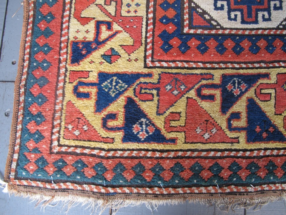 An antique hand-knotted wool Caucasian rug runner featuring a central column of stepped octagonal Memling guls on a red background bordered by geometric patterns. View V