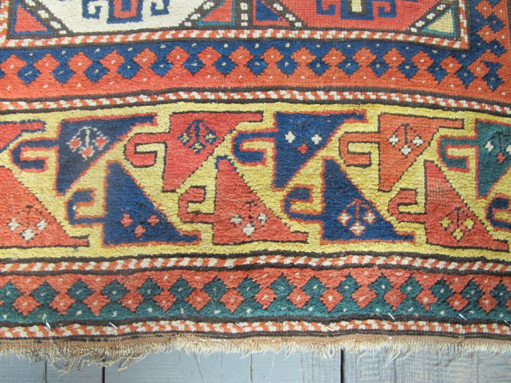 An antique hand-knotted wool Caucasian rug runner featuring a central column of stepped octagonal Memling guls on a red background bordered by geometric patterns. View VI
