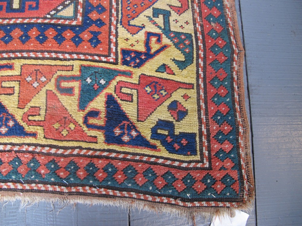 An antique hand-knotted wool Caucasian rug runner featuring a central column of stepped octagonal Memling guls on a red background bordered by geometric patterns. View VII
