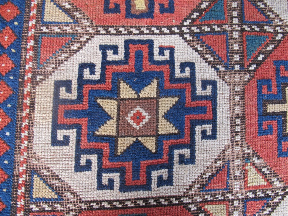An antique hand-knotted wool Caucasian rug runner featuring a central column of stepped octagonal Memling guls on a red background bordered by geometric patterns. View VIII