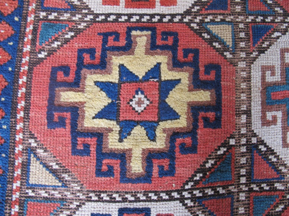 An antique hand-knotted wool Caucasian rug runner featuring a central column of stepped octagonal Memling guls on a red background bordered by geometric patterns. View IX