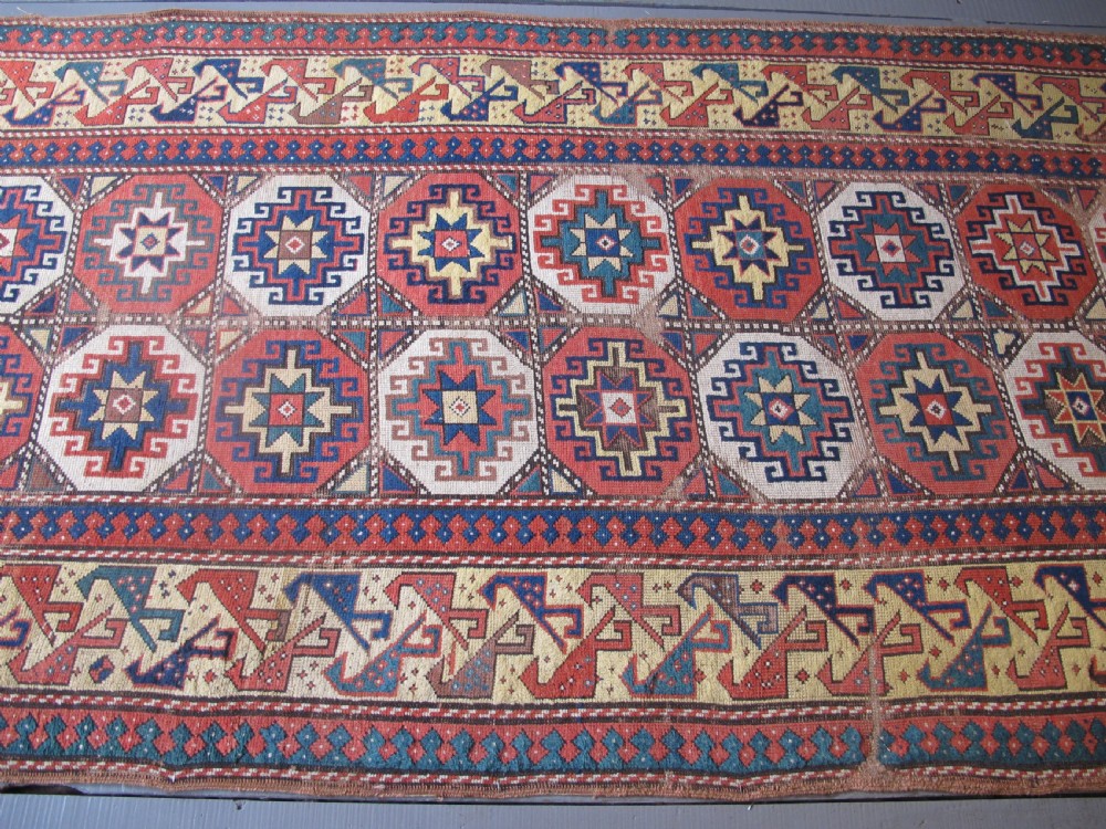 An antique hand-knotted wool Caucasian rug runner featuring a central column of stepped octagonal Memling guls on a red background bordered by geometric patterns. View XI