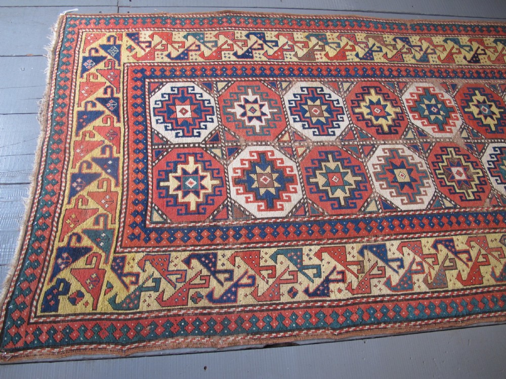 An antique hand-knotted wool Caucasian rug runner featuring a central column of stepped octagonal Memling guls on a red background bordered by geometric patterns. View XII