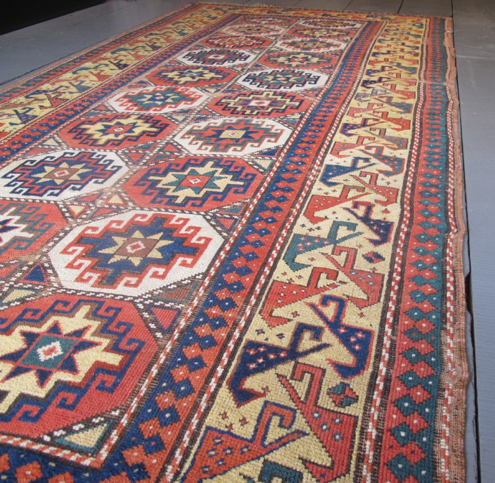 An antique hand-knotted wool Caucasian rug runner featuring a central column of stepped octagonal Memling guls on a red background bordered by geometric patterns. View XIII