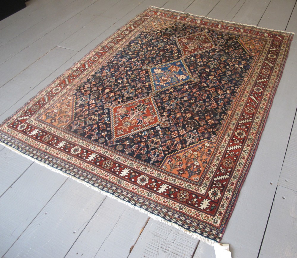 A hand-knotted Persian Qashqai wool rug featuring a dark navy field with central diamond medallions, geometric floral motifs, and a multi-tiered decorative border. View III
