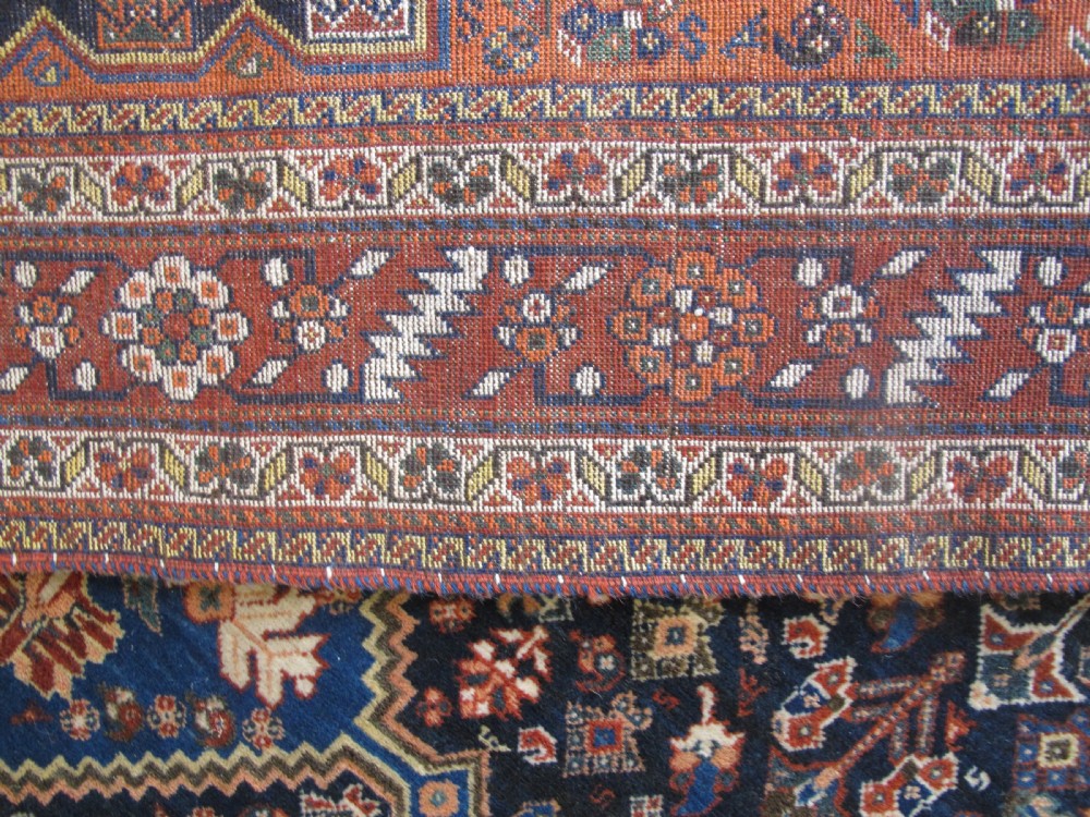 A hand-knotted Persian Qashqai wool rug featuring a dark navy field with central diamond medallions, geometric floral motifs, and a multi-tiered decorative border. View VIII