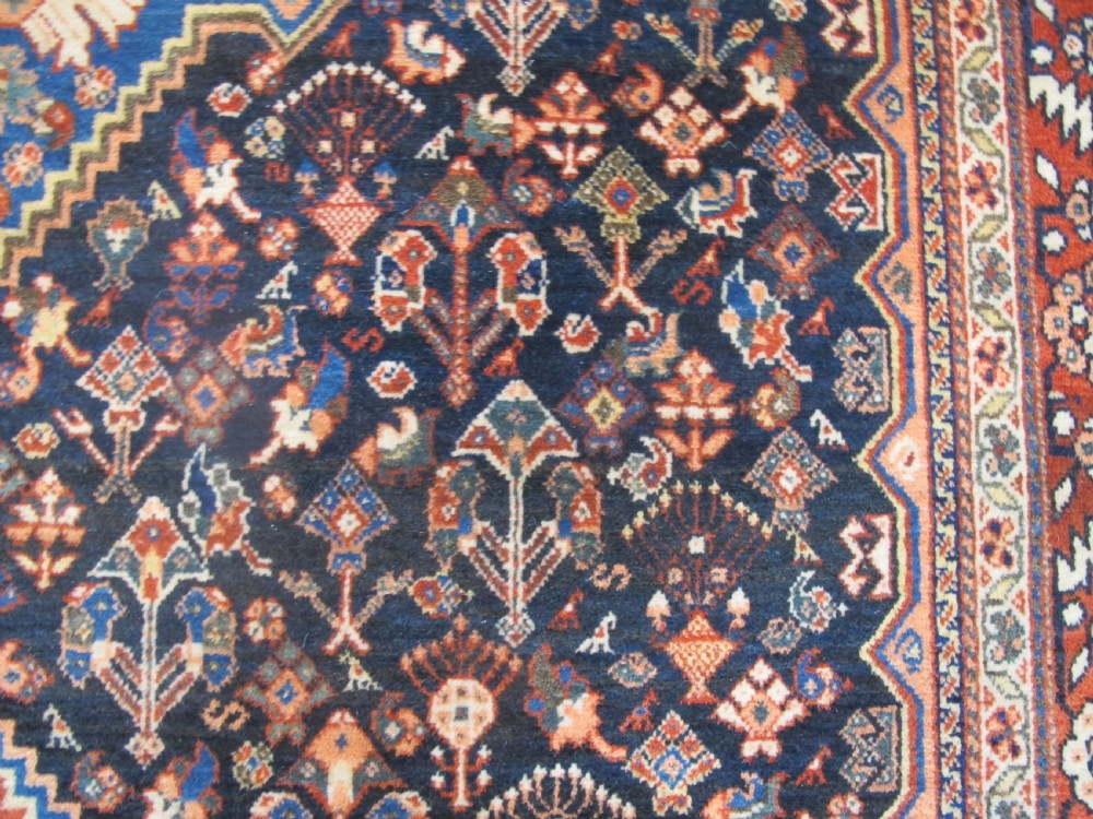 A hand-knotted Persian Qashqai wool rug featuring a dark navy field with central diamond medallions, geometric floral motifs, and a multi-tiered decorative border. View XI