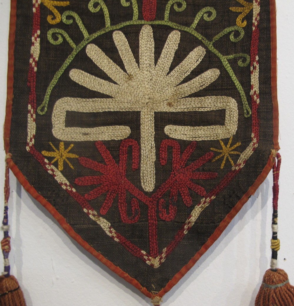 An antique Uzbek vertical silk embroidered textile amulet featuring yellow, red, and cream palmette motifs on a dark brown ground with hanging tassels. View II