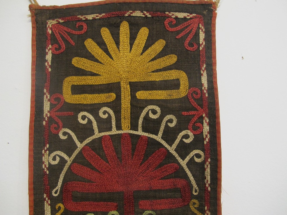 An antique Uzbek vertical silk embroidered textile amulet featuring yellow, red, and cream palmette motifs on a dark brown ground with hanging tassels. View III
