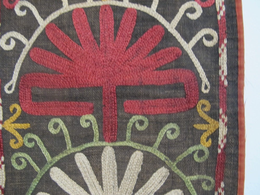 An antique Uzbek vertical silk embroidered textile amulet featuring yellow, red, and cream palmette motifs on a dark brown ground with hanging tassels. View IV