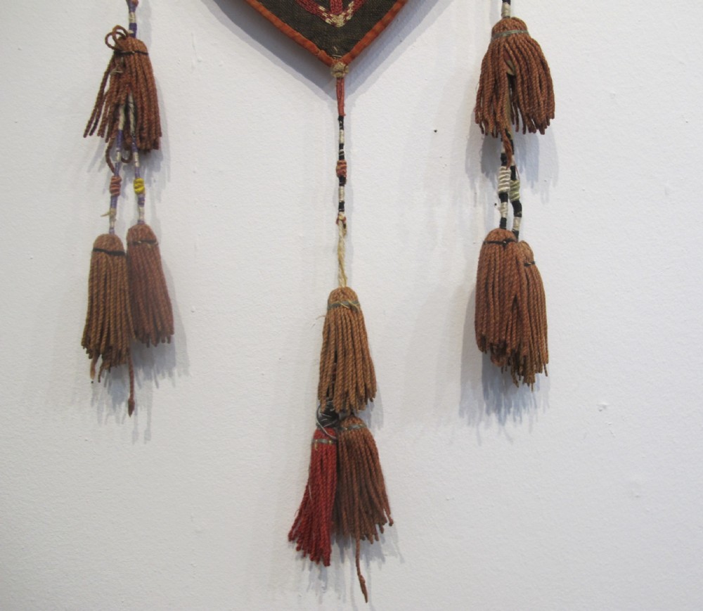 An antique Uzbek vertical silk embroidered textile amulet featuring yellow, red, and cream palmette motifs on a dark brown ground with hanging tassels. View V
