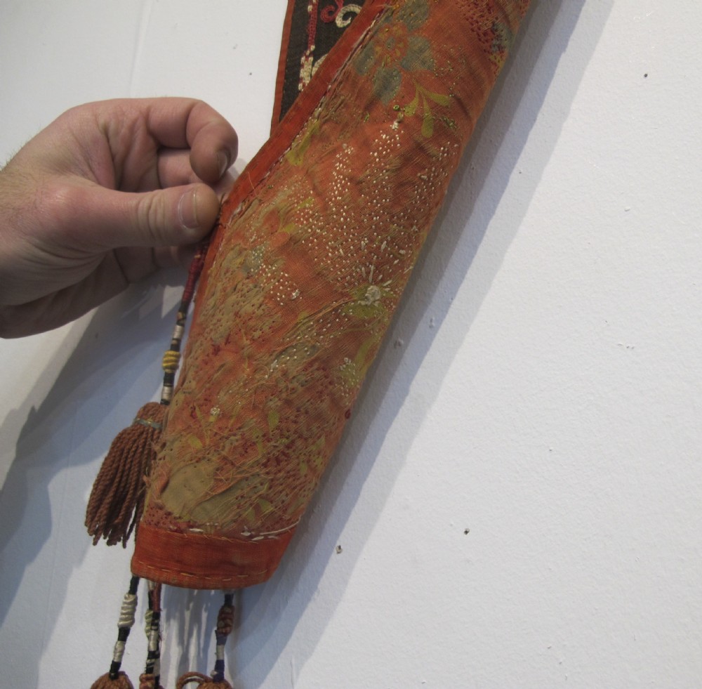 An antique Uzbek vertical silk embroidered textile amulet featuring yellow, red, and cream palmette motifs on a dark brown ground with hanging tassels. View VI
