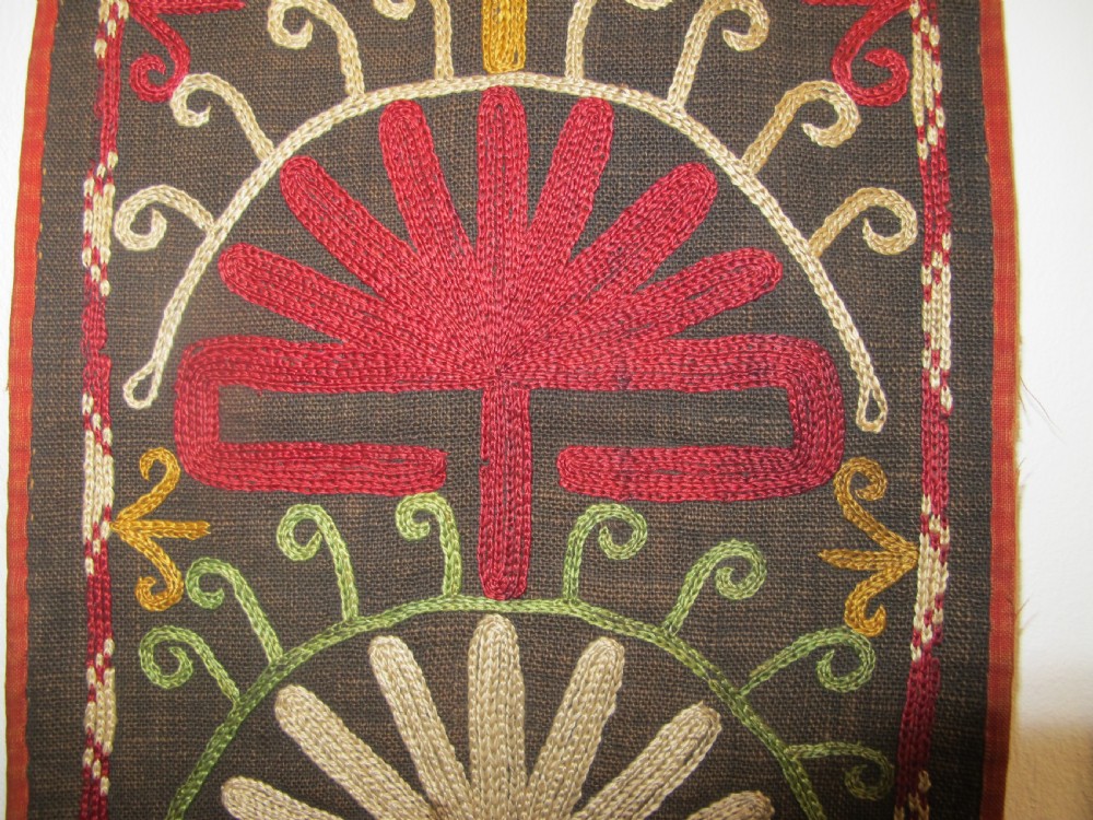 An antique Uzbek vertical silk embroidered textile amulet featuring yellow, red, and cream palmette motifs on a dark brown ground with hanging tassels. View VII