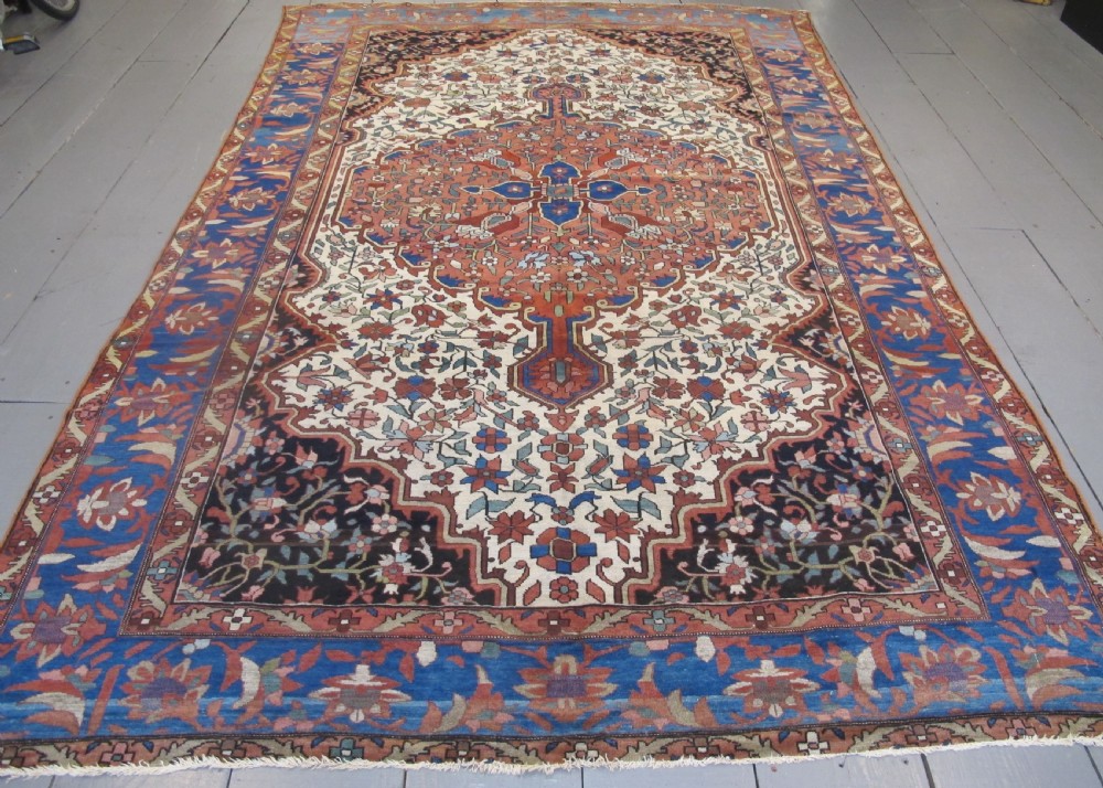 A late 19th-century hand-knotted Persian Melayir wool carpet featuring a large central terracotta medallion on a cream field framed by navy spandrels and a blue botanical border.