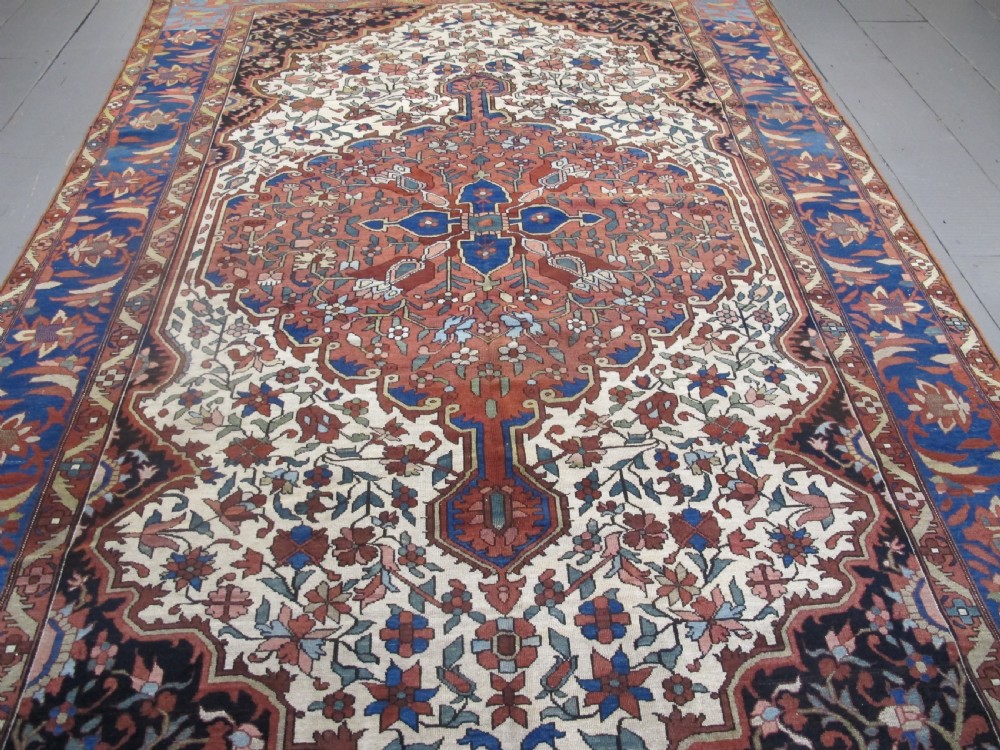 A late 19th-century hand-knotted Persian Melayir wool carpet featuring a large central terracotta medallion on a cream field framed by navy spandrels and a blue botanical border. View II
