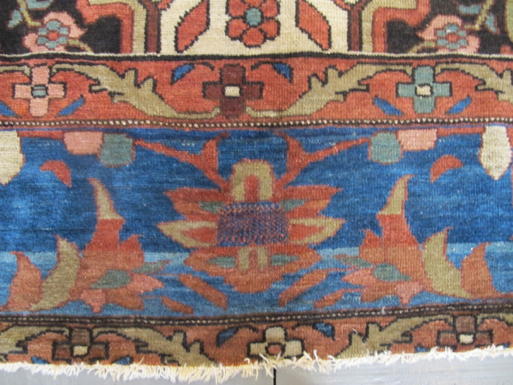 A late 19th-century hand-knotted Persian Melayir wool carpet featuring a large central terracotta medallion on a cream field framed by navy spandrels and a blue botanical border. View VI