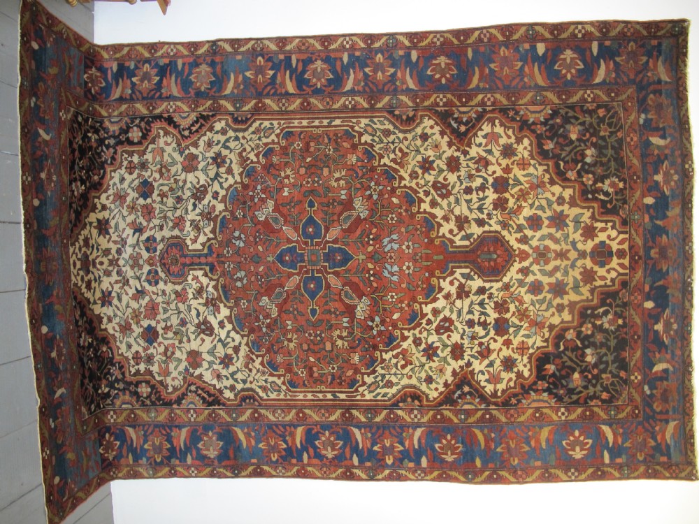 A late 19th-century hand-knotted Persian Melayir wool carpet featuring a large central terracotta medallion on a cream field framed by navy spandrels and a blue botanical border. View IX