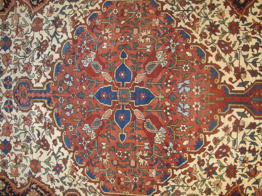 A late 19th-century hand-knotted Persian Melayir wool carpet featuring a large central terracotta medallion on a cream field framed by navy spandrels and a blue botanical border. View X