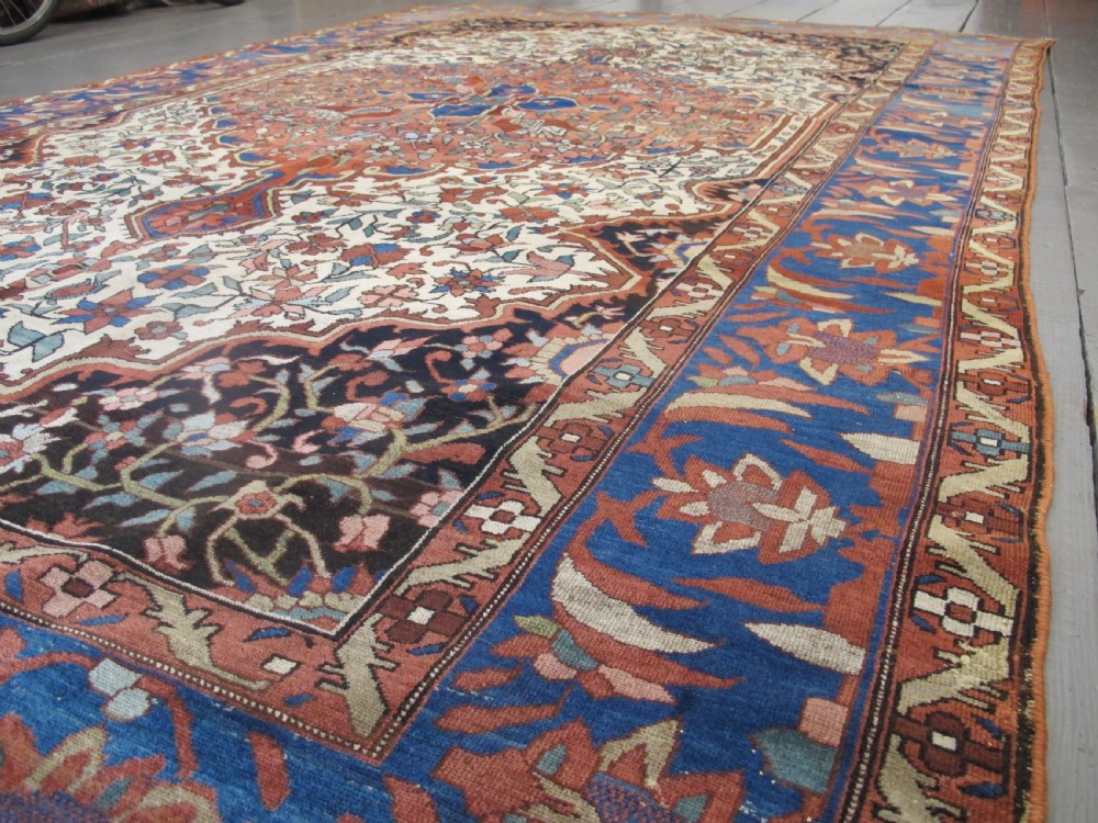 A late 19th-century hand-knotted Persian Melayir wool carpet featuring a large central terracotta medallion on a cream field framed by navy spandrels and a blue botanical border. View XII