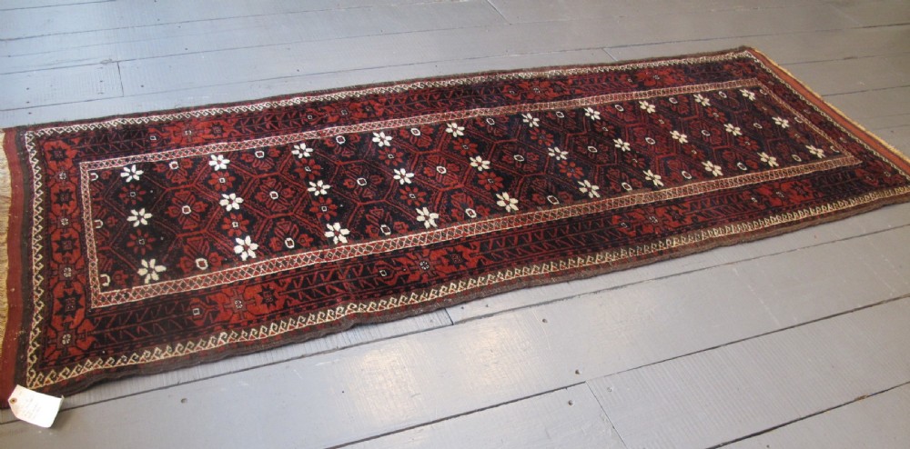 An antique Balouchi handwoven wool runner rug displaying repeating geometric star motifs in deep red, navy, and ivory tones on a dark background.