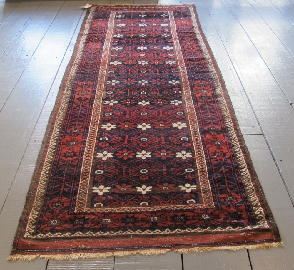 An antique Balouchi handwoven wool runner rug displaying repeating geometric star motifs in deep red, navy, and ivory tones on a dark background. View II