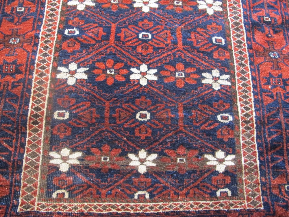 An antique Balouchi handwoven wool runner rug displaying repeating geometric star motifs in deep red, navy, and ivory tones on a dark background. View III