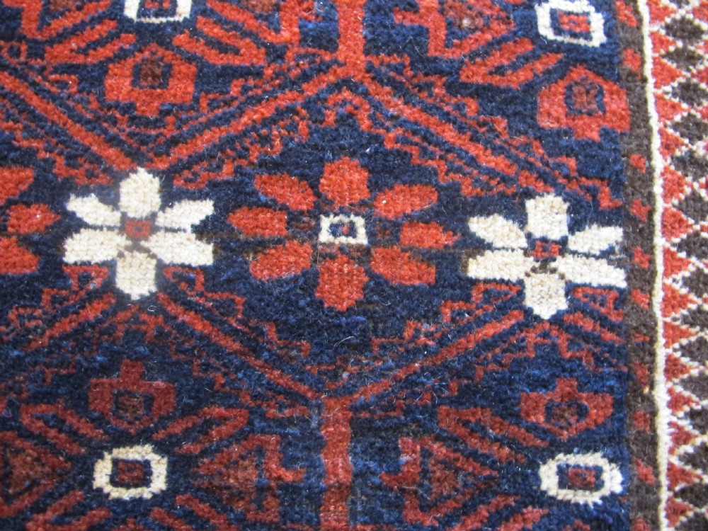 An antique Balouchi handwoven wool runner rug displaying repeating geometric star motifs in deep red, navy, and ivory tones on a dark background. View V