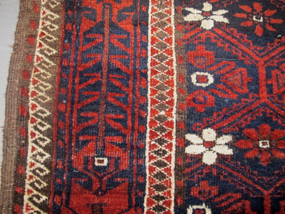 An antique Balouchi handwoven wool runner rug displaying repeating geometric star motifs in deep red, navy, and ivory tones on a dark background. View VI